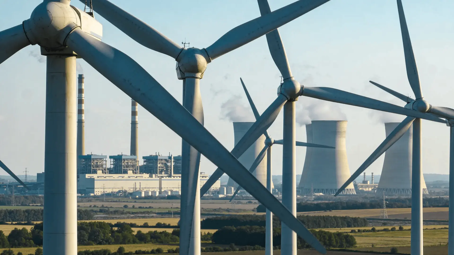 Wind turbines in a field with a distant fossil fuel power plant in the background