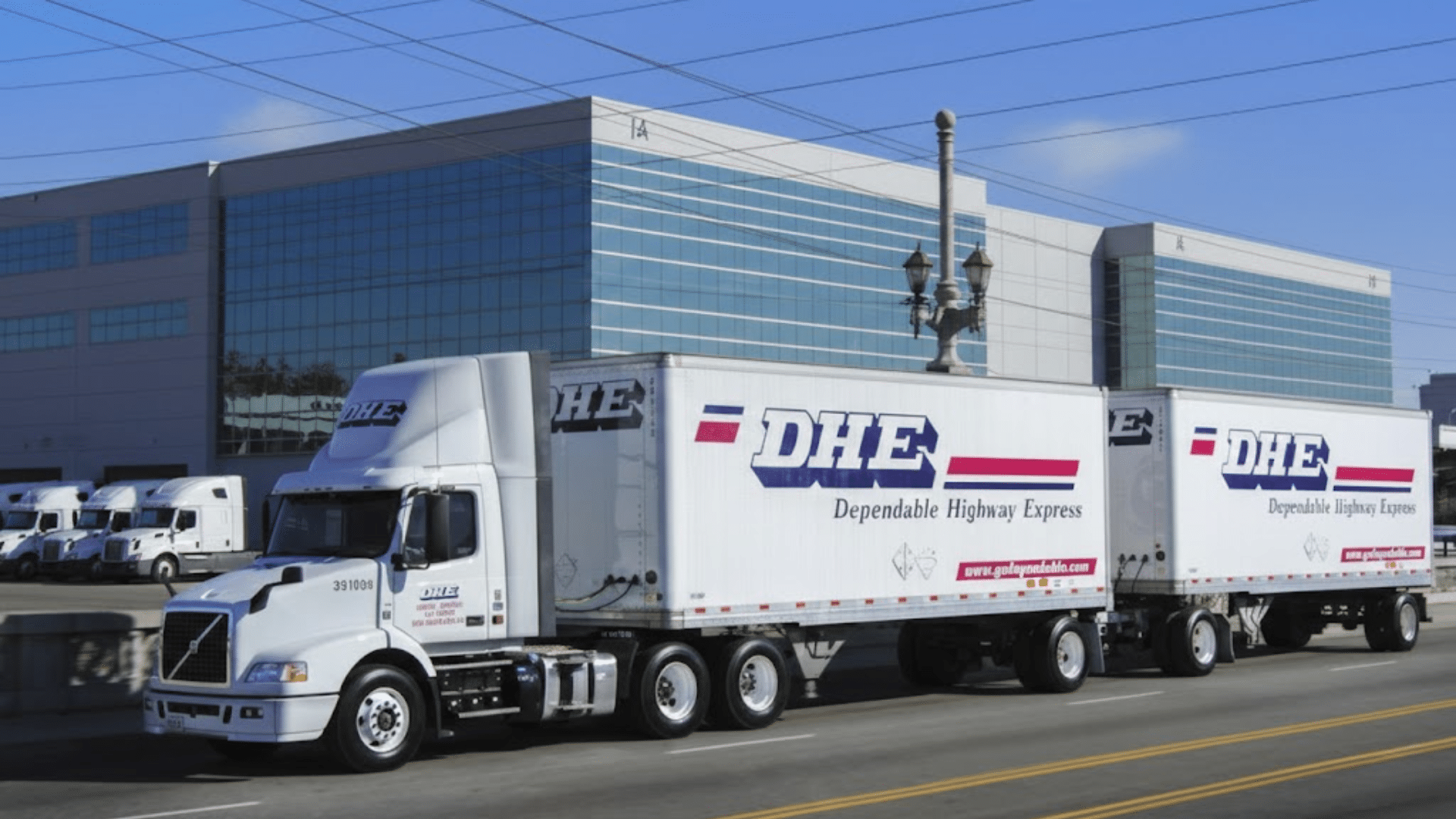 dhe dependable highway express semi truck with double trailers driving past modern warehouse building on city street