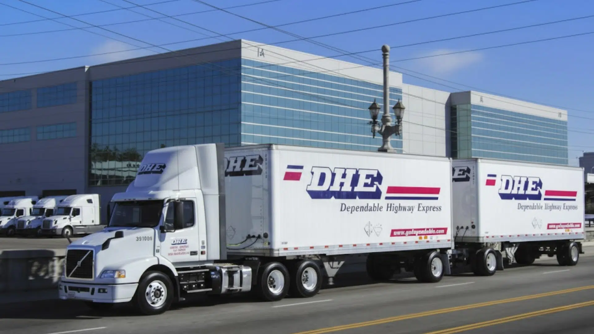 dhe dependable highway express semi truck with double trailers driving past modern warehouse building on city street