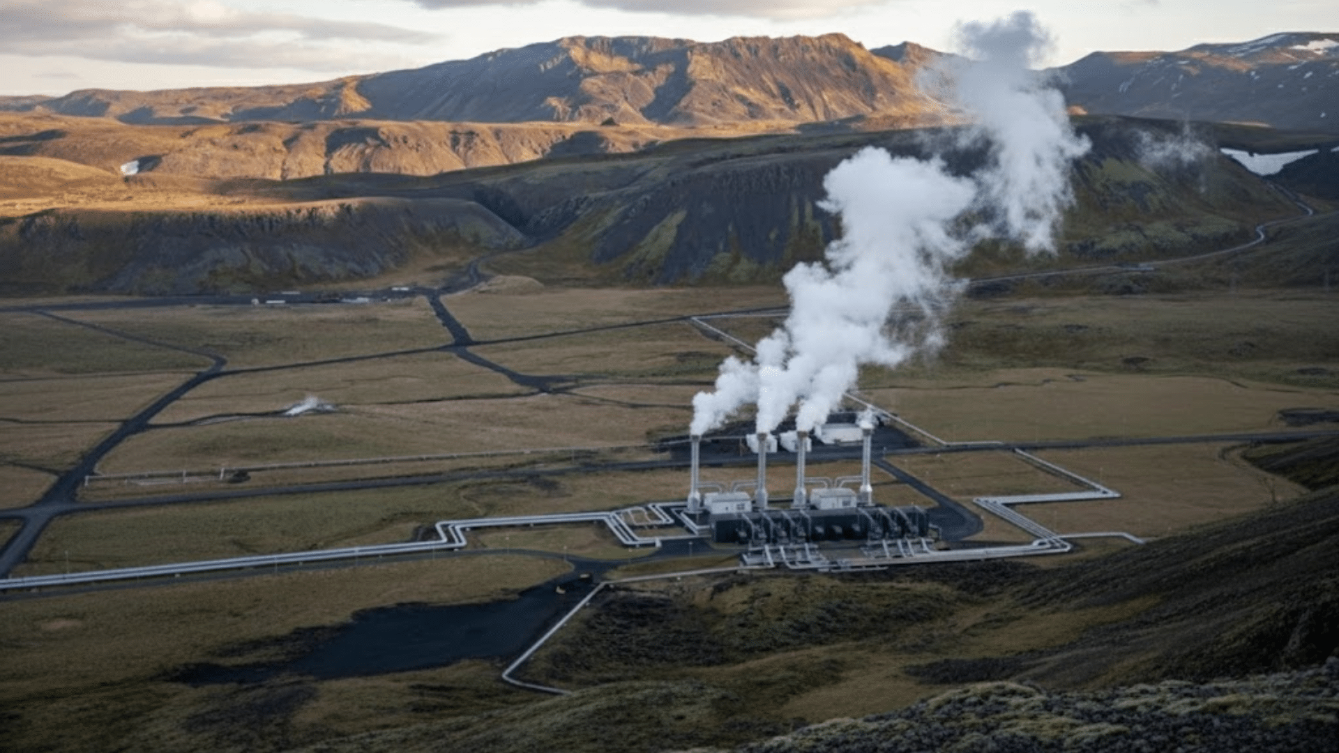 geothermal power plant with steam rising from cooling towers in a wide valley surrounded by mountains and open land