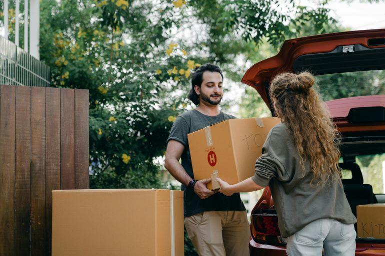 Man and woman lifting cardboard boxes into a car trunk during a home move.
