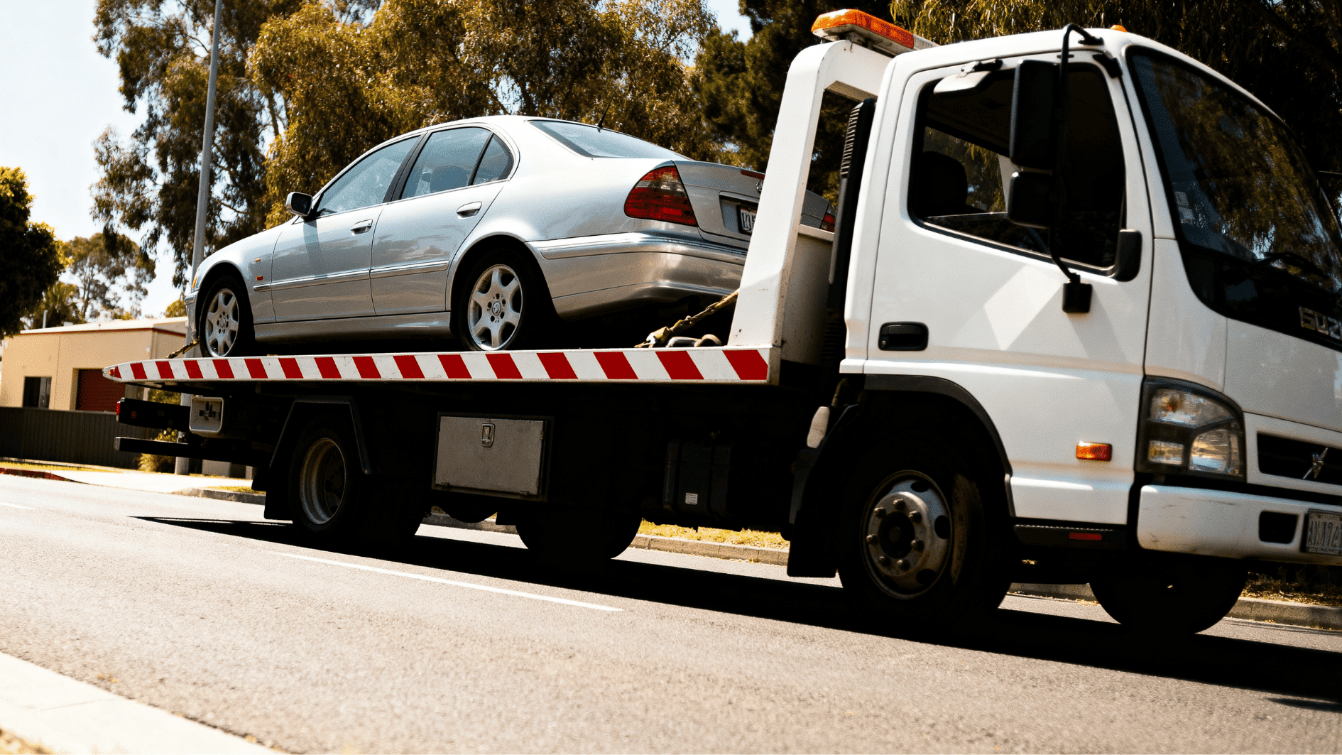 flatbed tow truck carrying a silver sedan on city street during daytime with secure vehicle transport in action