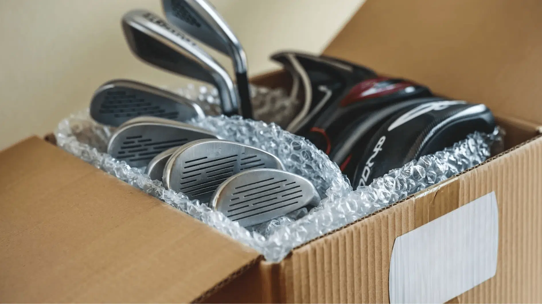 golf clubs wrapped in bubble wrap and packed inside a cardboard box for safe shipping with golf bag and protective packaging materials