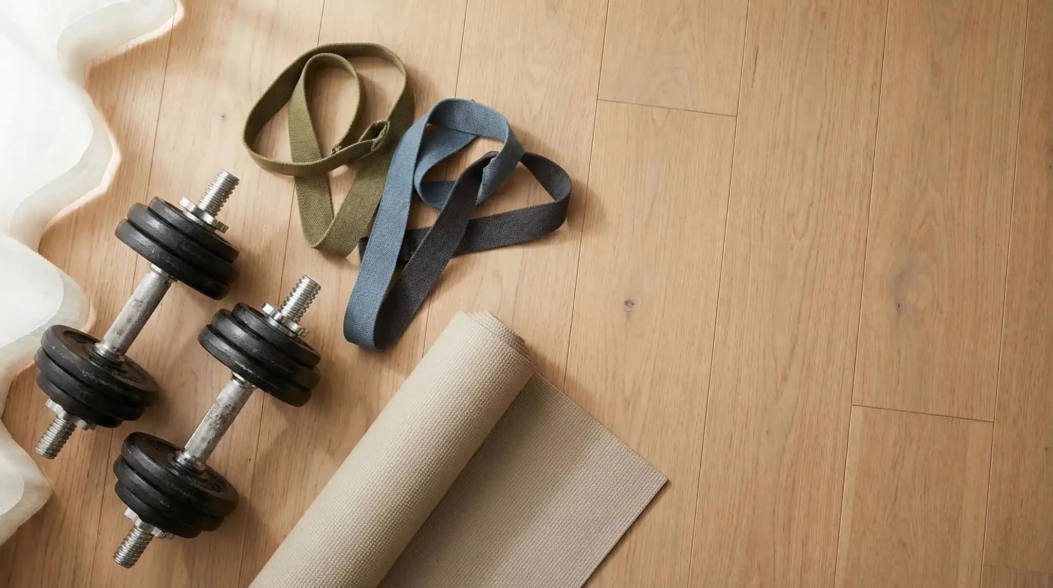 Dumbbells, fitness bands, and yoga mat on light wood floor in natural daylight