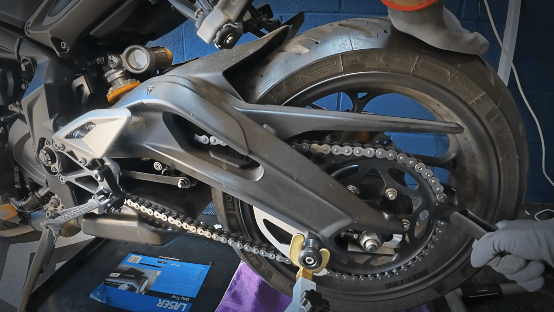 motorcycle chain being lubricated and adjusted to prevent rust and wear before winter storage period