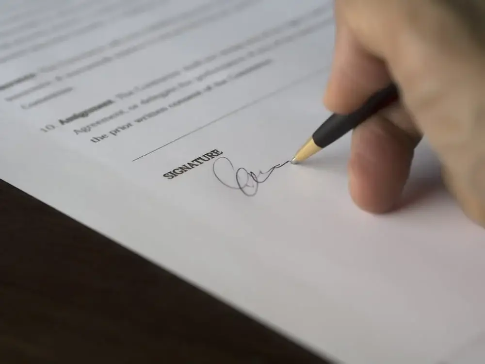 Hand signing a document with a black pen on a wooden desk