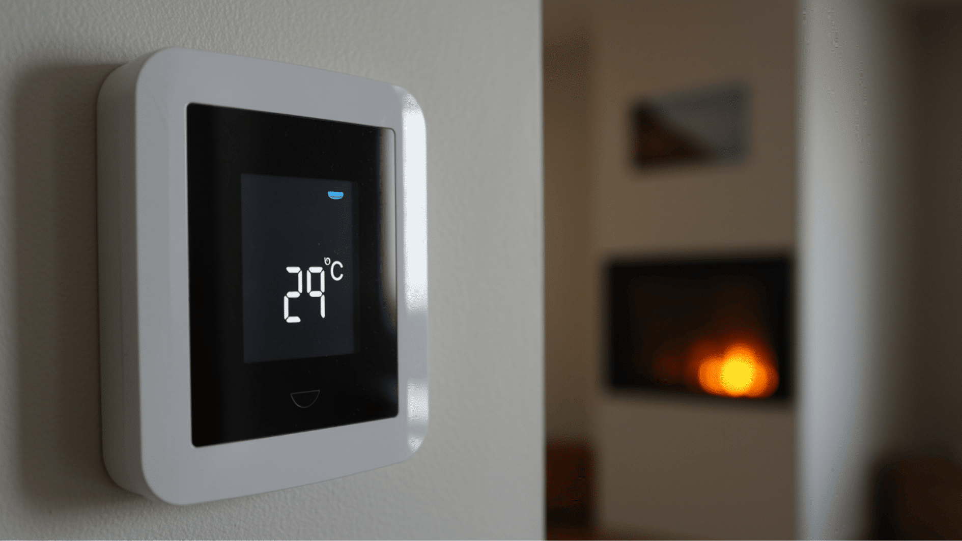 wall-mounted digital thermostat showing 29°C, with a warm fireplace softly blurred in the background.