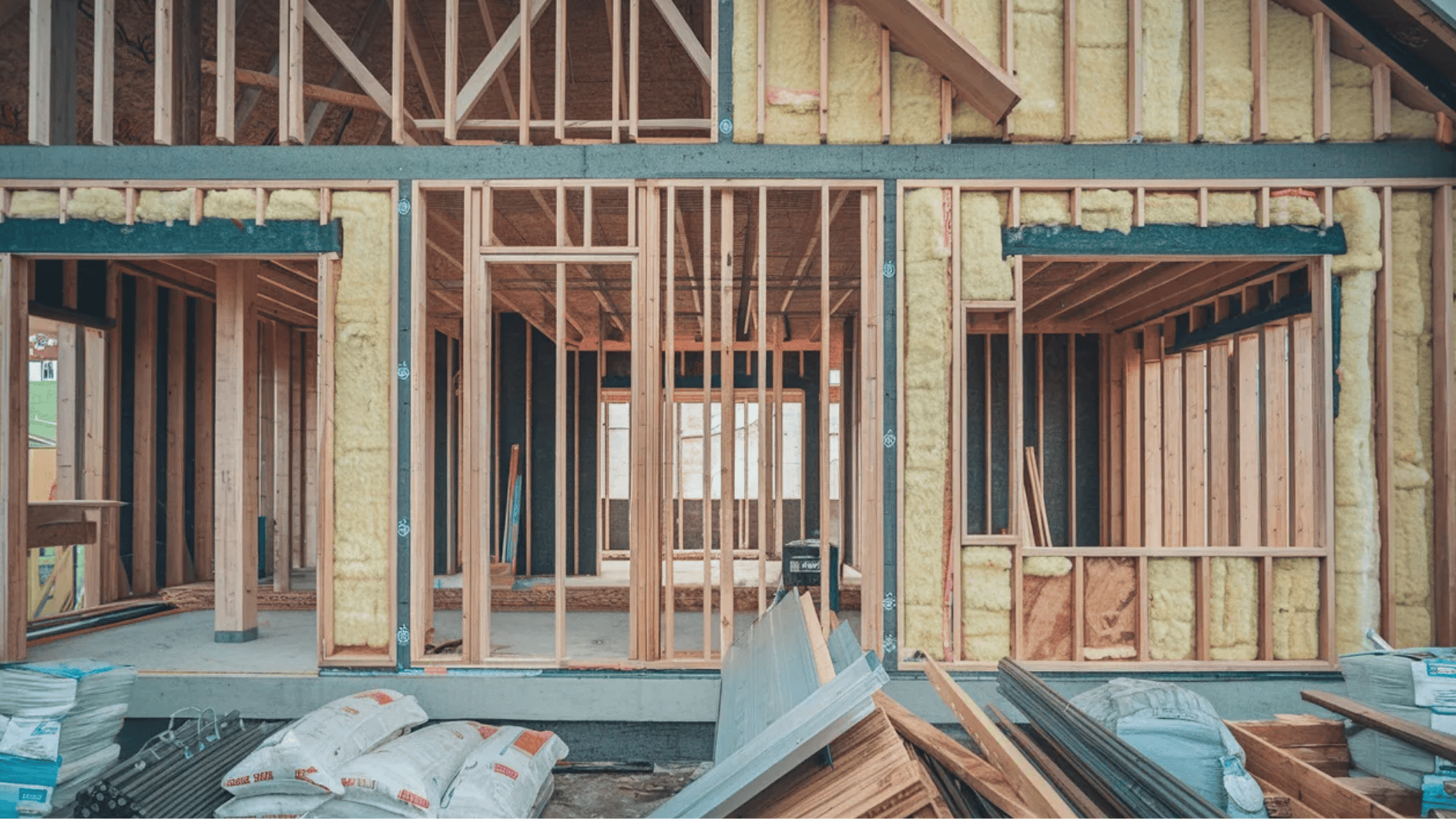 wood-framed house under construction with exposed studs, insulation, and building materials on site