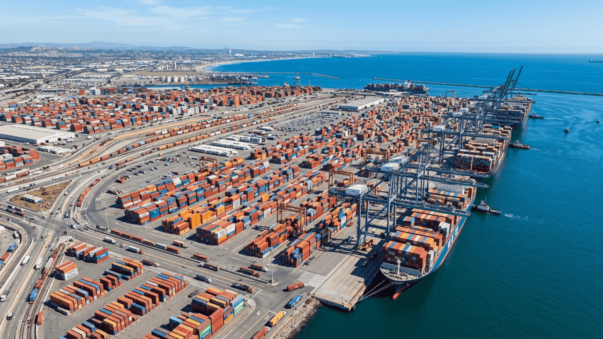 aerial view of busy seaport with shipping containers, cranes, and coastline