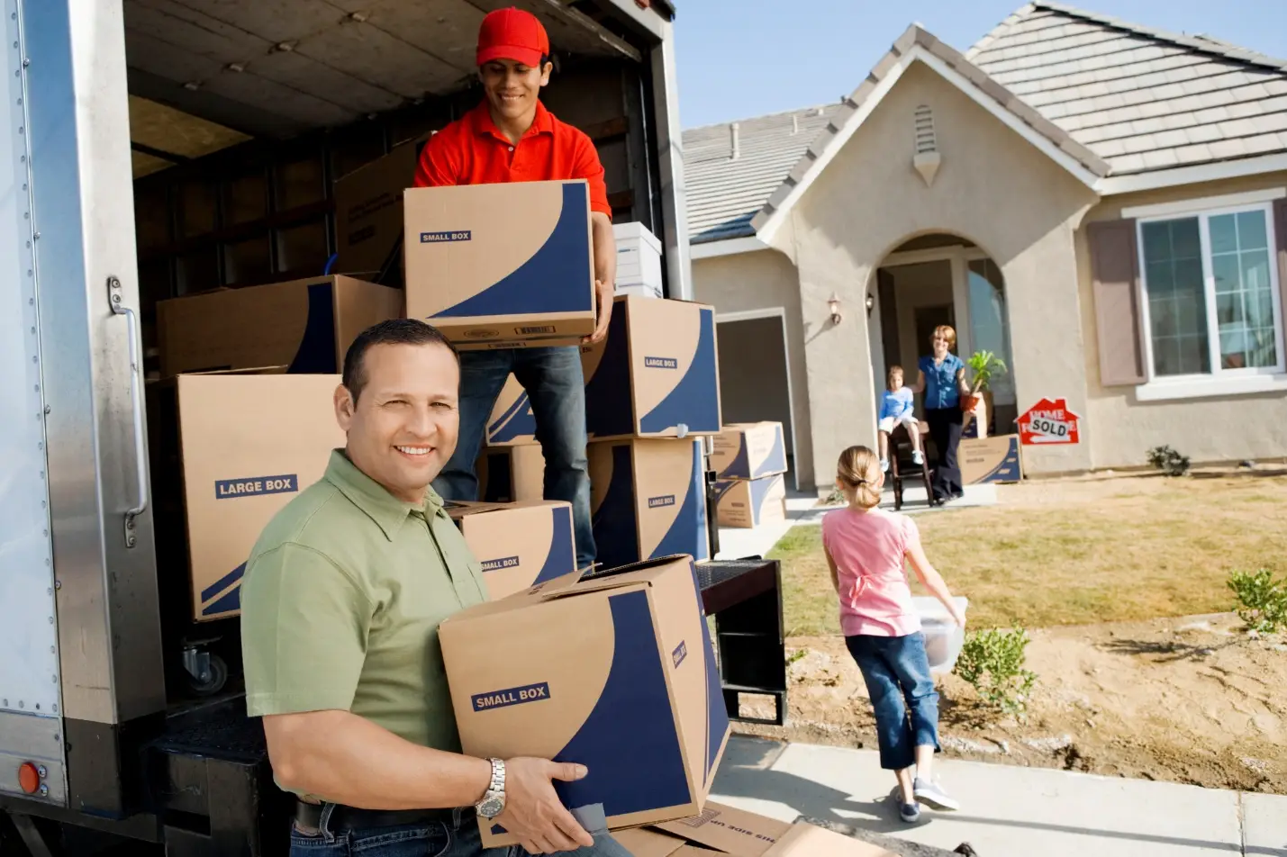 People unloading cardboard boxes from a moving truck in front of a new home