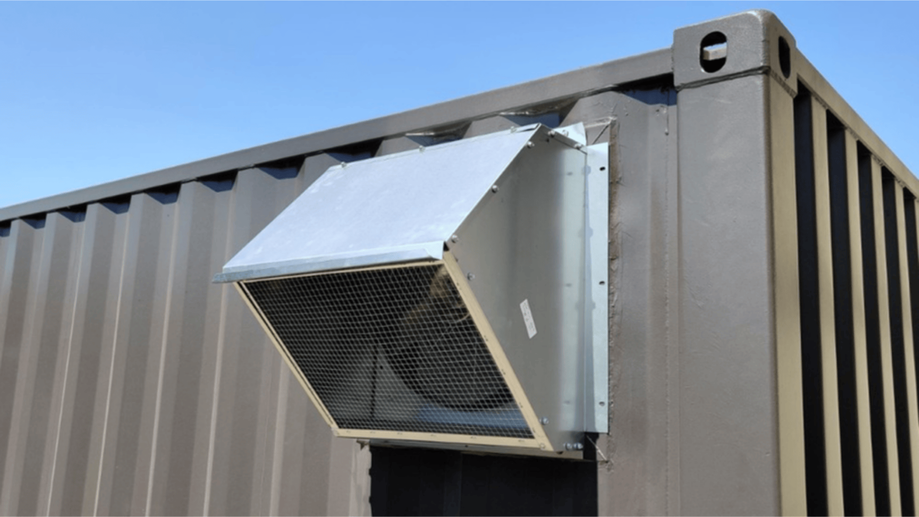 exterior ventilation unit mounted on shipping container wall with protective hood and mesh cover for airflow system