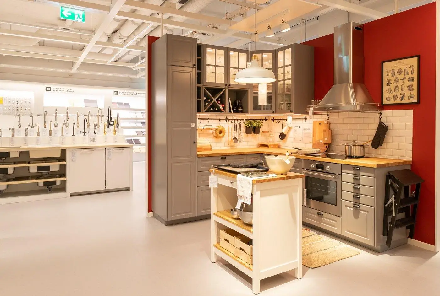 Modern kitchen showroom with gray cabinets, red accent wall, and stainless steel appliances