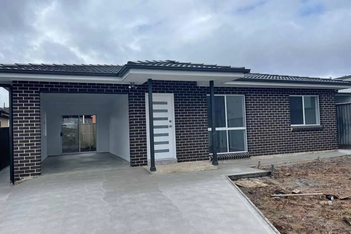 Newly constructed brick house with carport and clean concrete driveway under cloudy sky