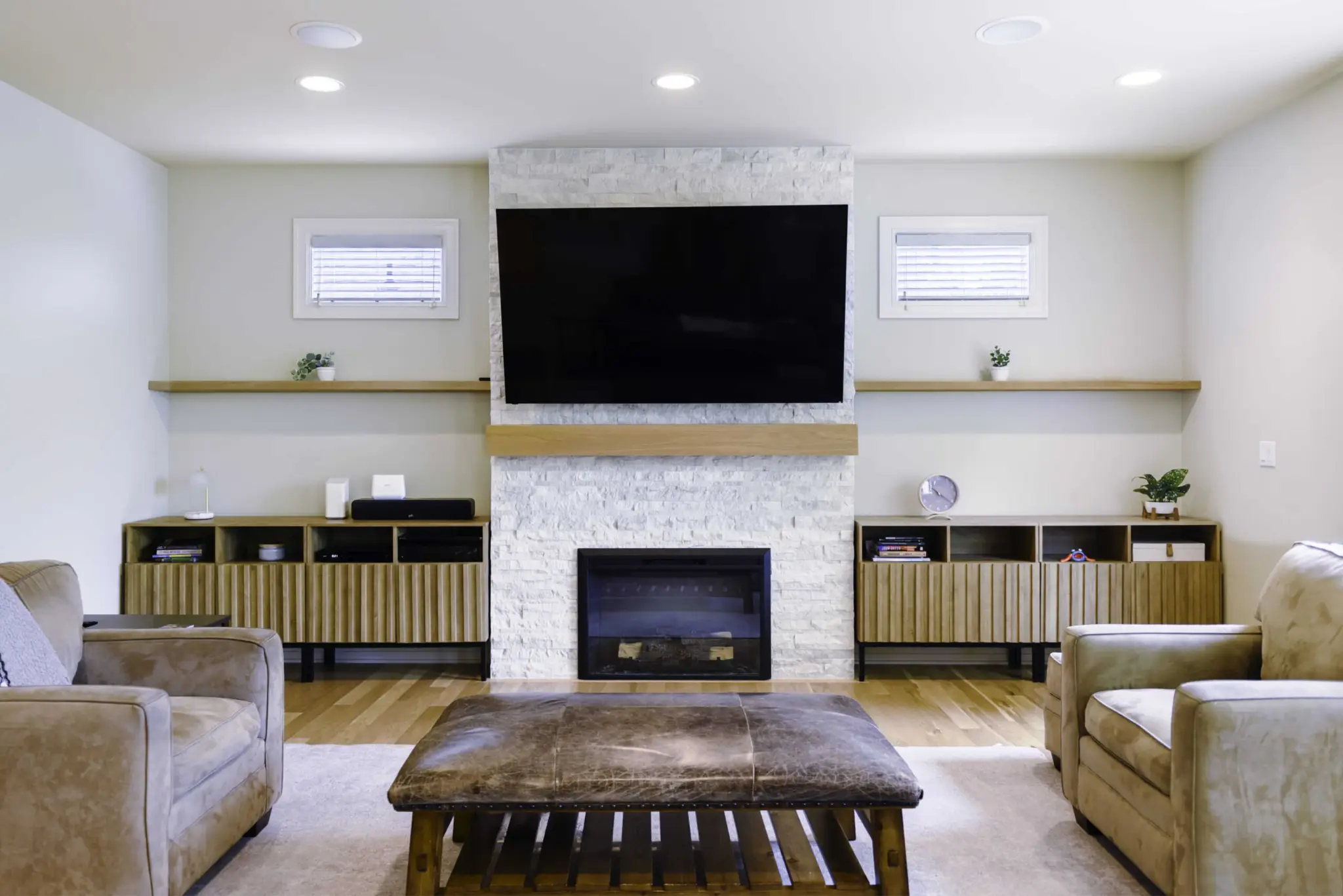 Modern living room with large TV above stone fireplace, beige sofas, and wooden furniture