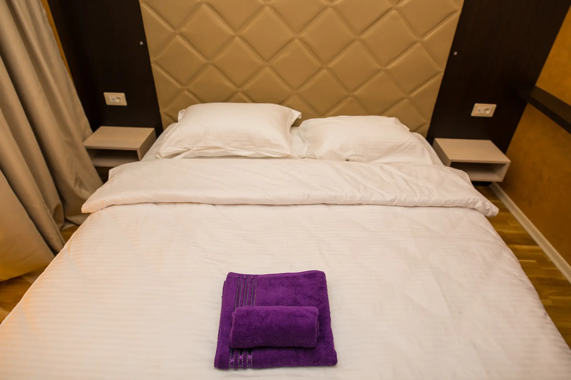 Neatly arranged bed with white linens and purple towels in a hotel room setting