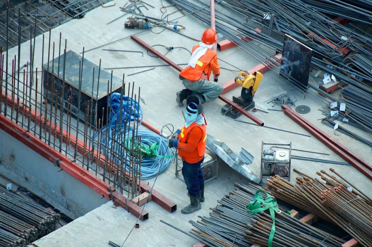 Construction workers in safety gear on site with rebar and tools scattered around