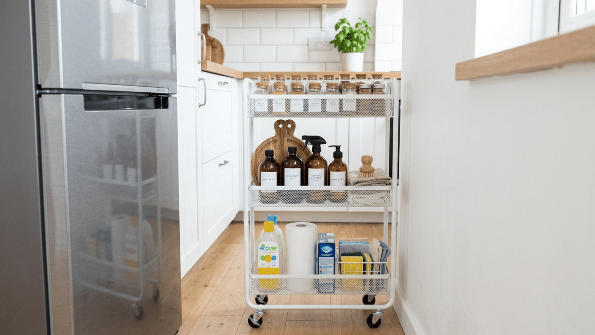 narrow white rolling cart tucked between refrigerator and wall holding kitchen supplies