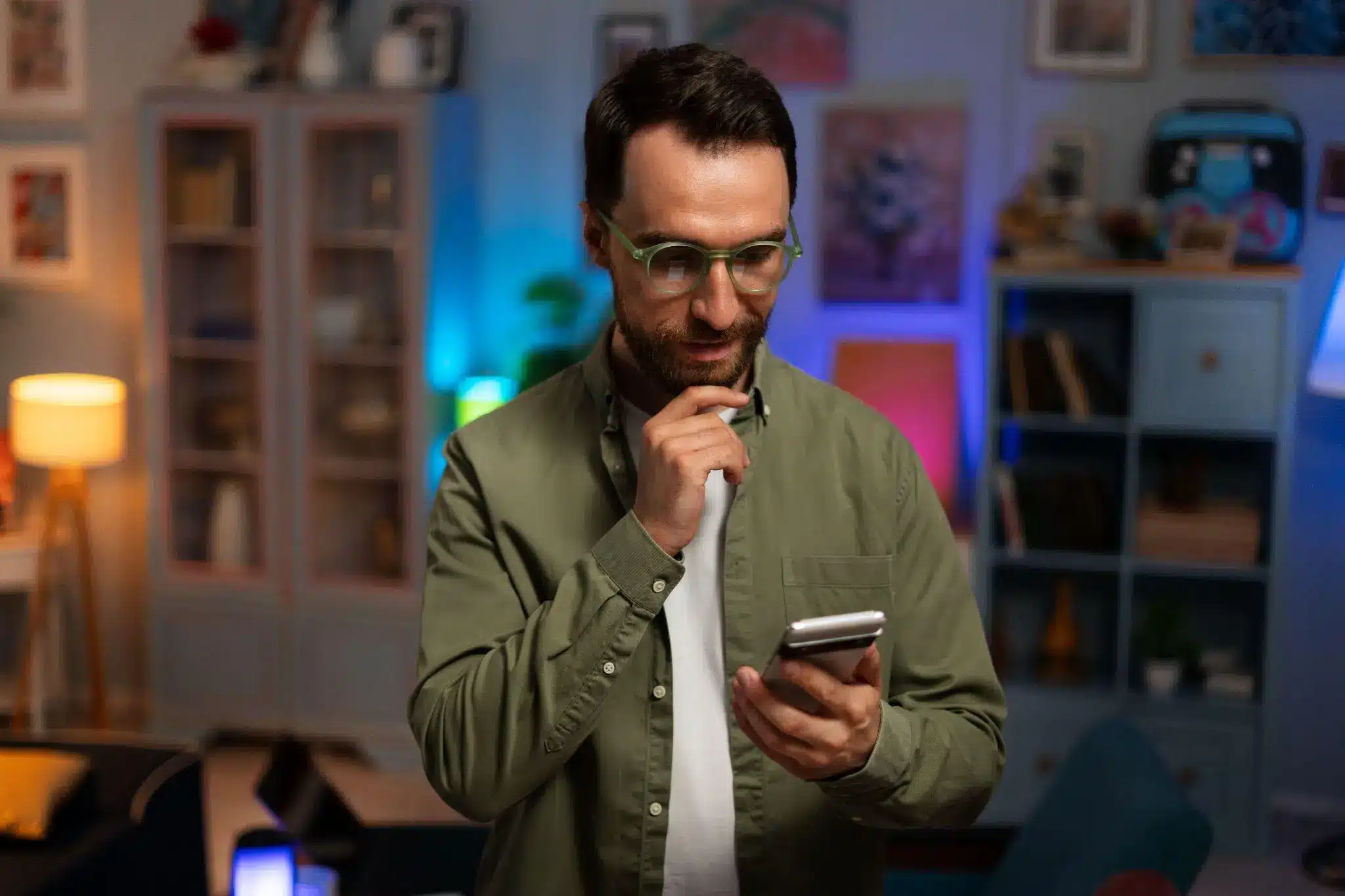 Man in glasses using smartphone thoughtfully in cozy, dimly lit living room
