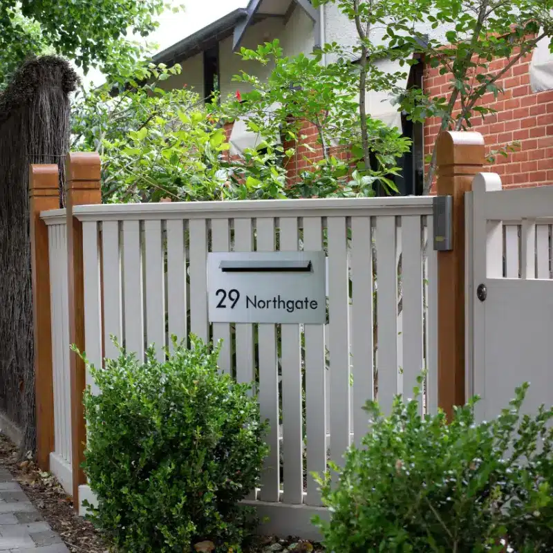 Residential front gate with address plaque surrounded by greenery and brick wall