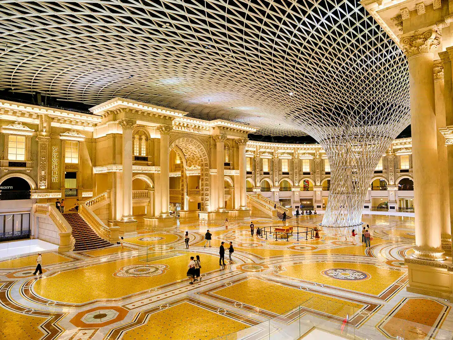 Ornate grand hall with intricate ceiling design and illuminated columns, featuring a central spiral art installation