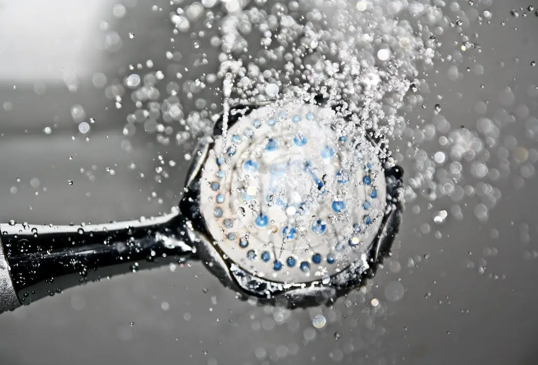 Showerhead releasing water spray in close-up with droplets and reflections in bright light