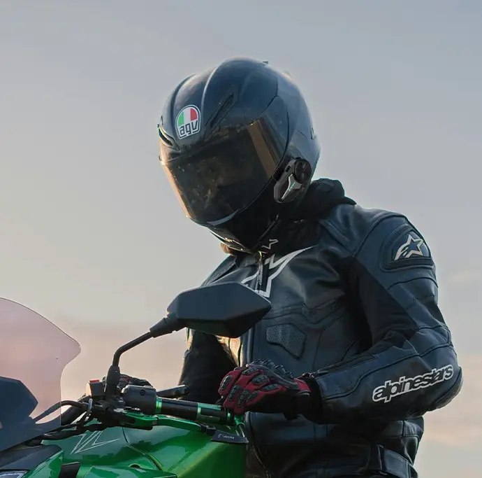 Motorcyclist in black leather gear riding green bike outdoors at sunset