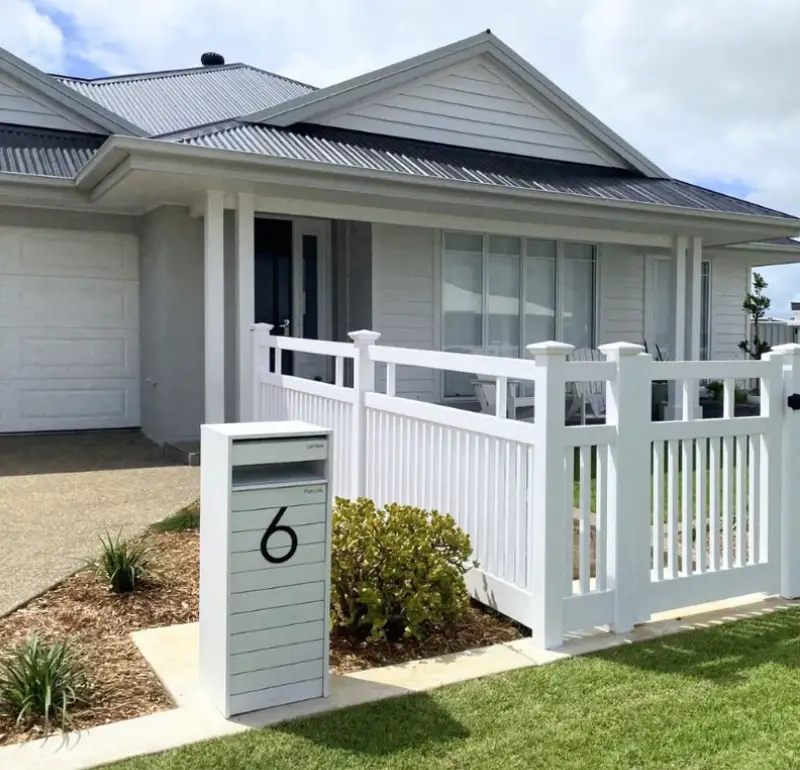 Modern suburban house with white picket fence and grey metal roof in a landscaped front yard