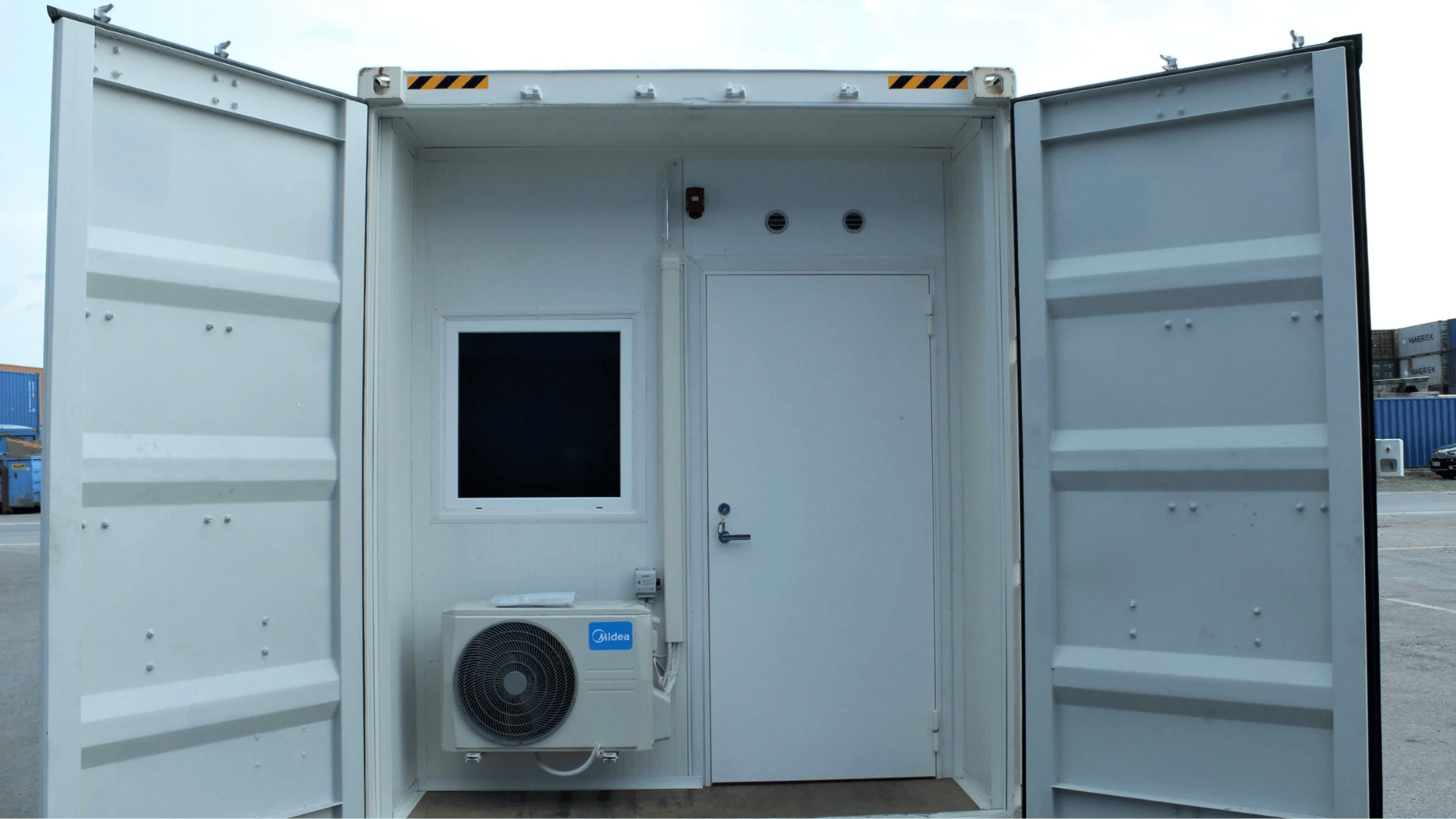 modified shipping container with open doors showing installed door, window, and external AC unit in industrial yard