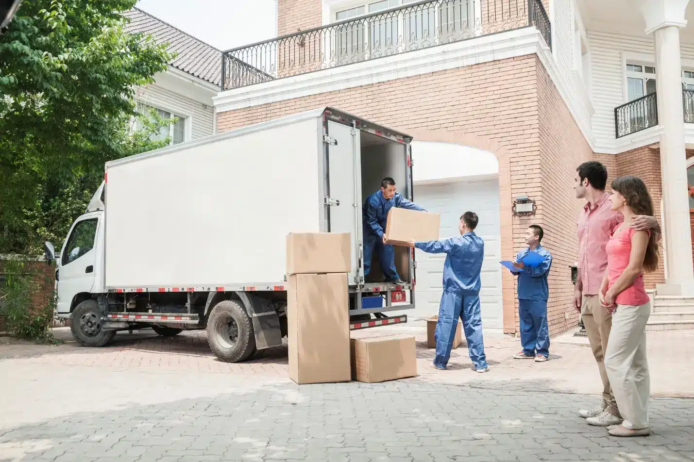 Movers unloading cardboard boxes from a truck in front of a brick house