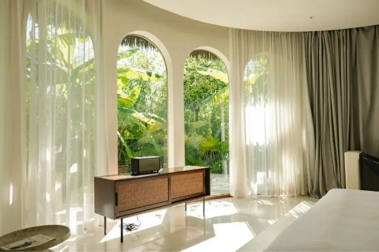 Mid-century modern room with large arched windows and lush garden view through sheer curtains
