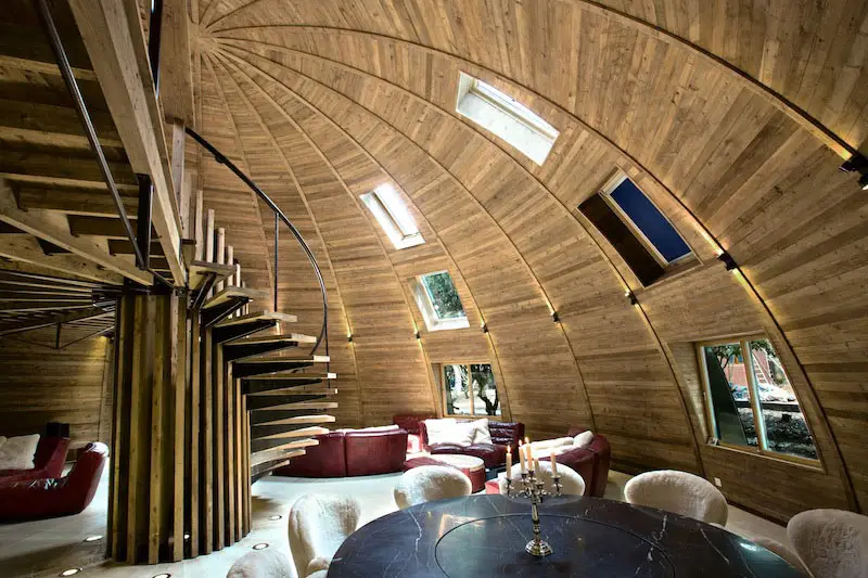 Wooden dome interior with spiral staircase, circular table, and red sofas under skylights
