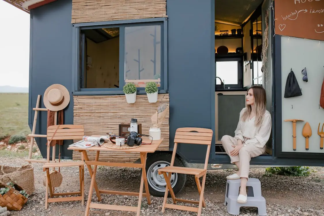 Woman sitting by a tiny house with folding chairs and gardening tools outdoors