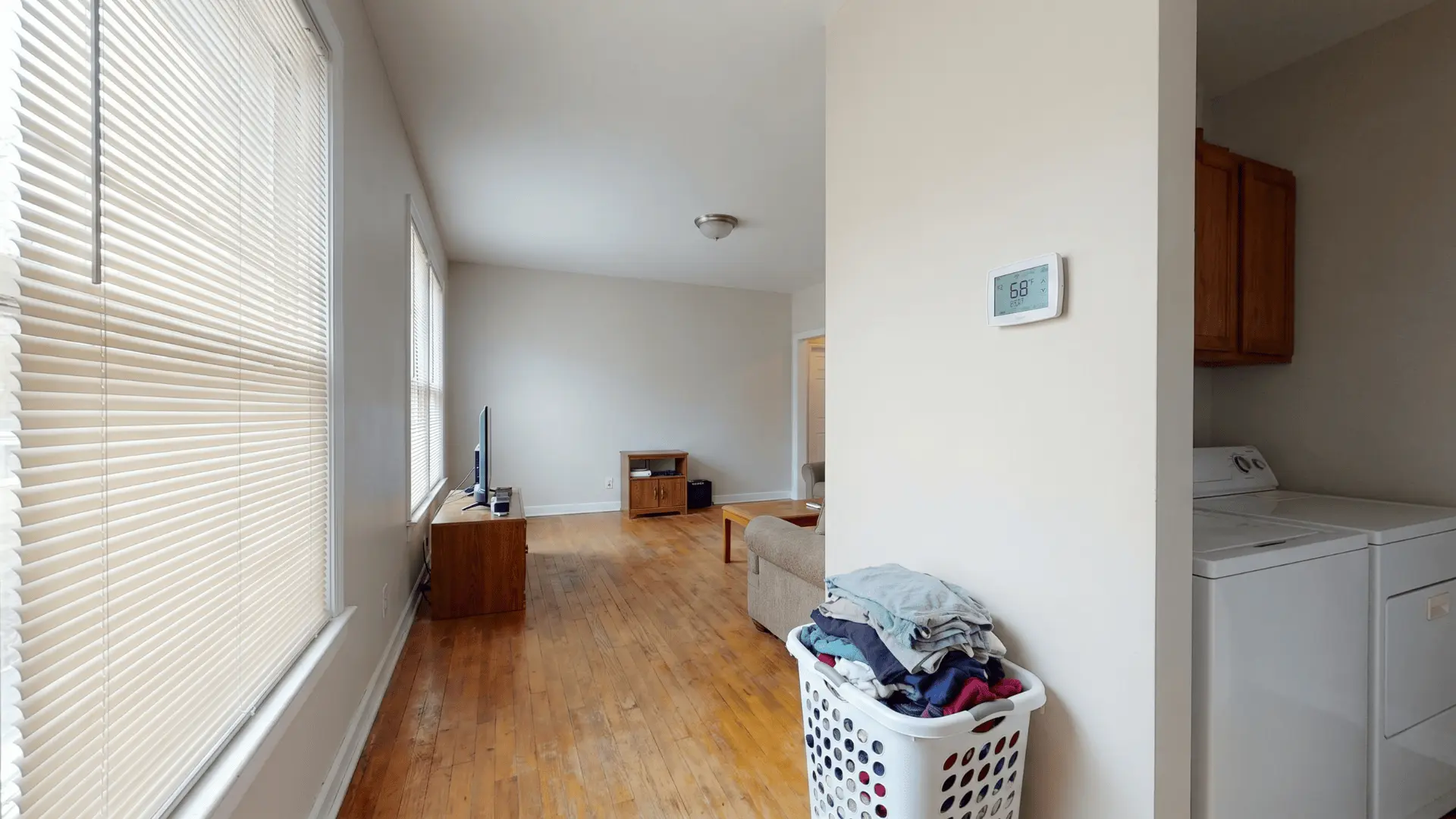 Thermostat, closed blinds, and a full laundry basket in a home interior