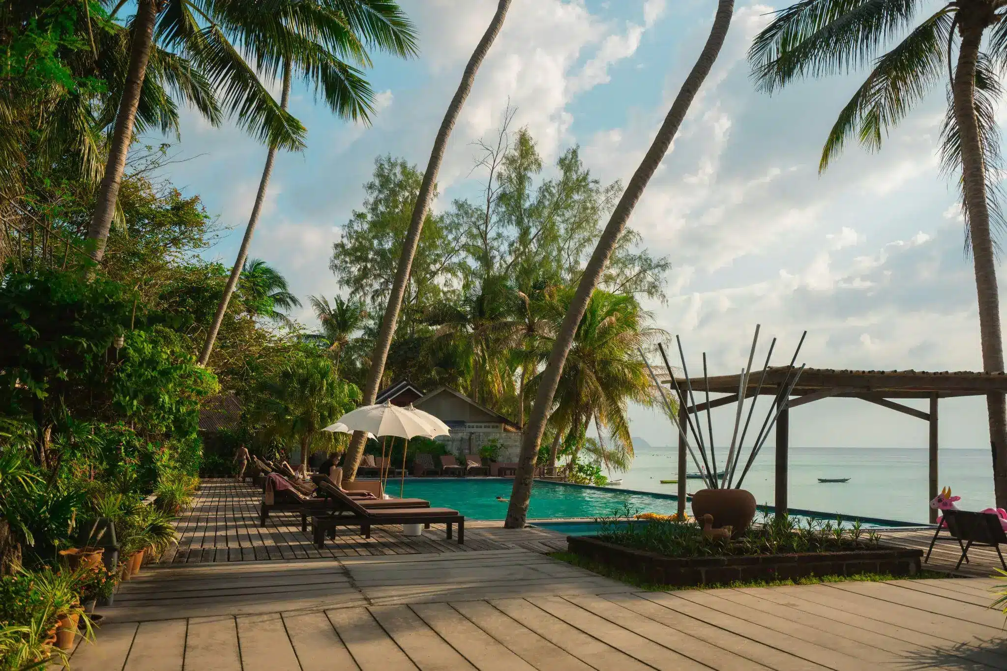 Tropical resort with wooden deck chairs and umbrella by oceanfront pool surrounded by palm trees