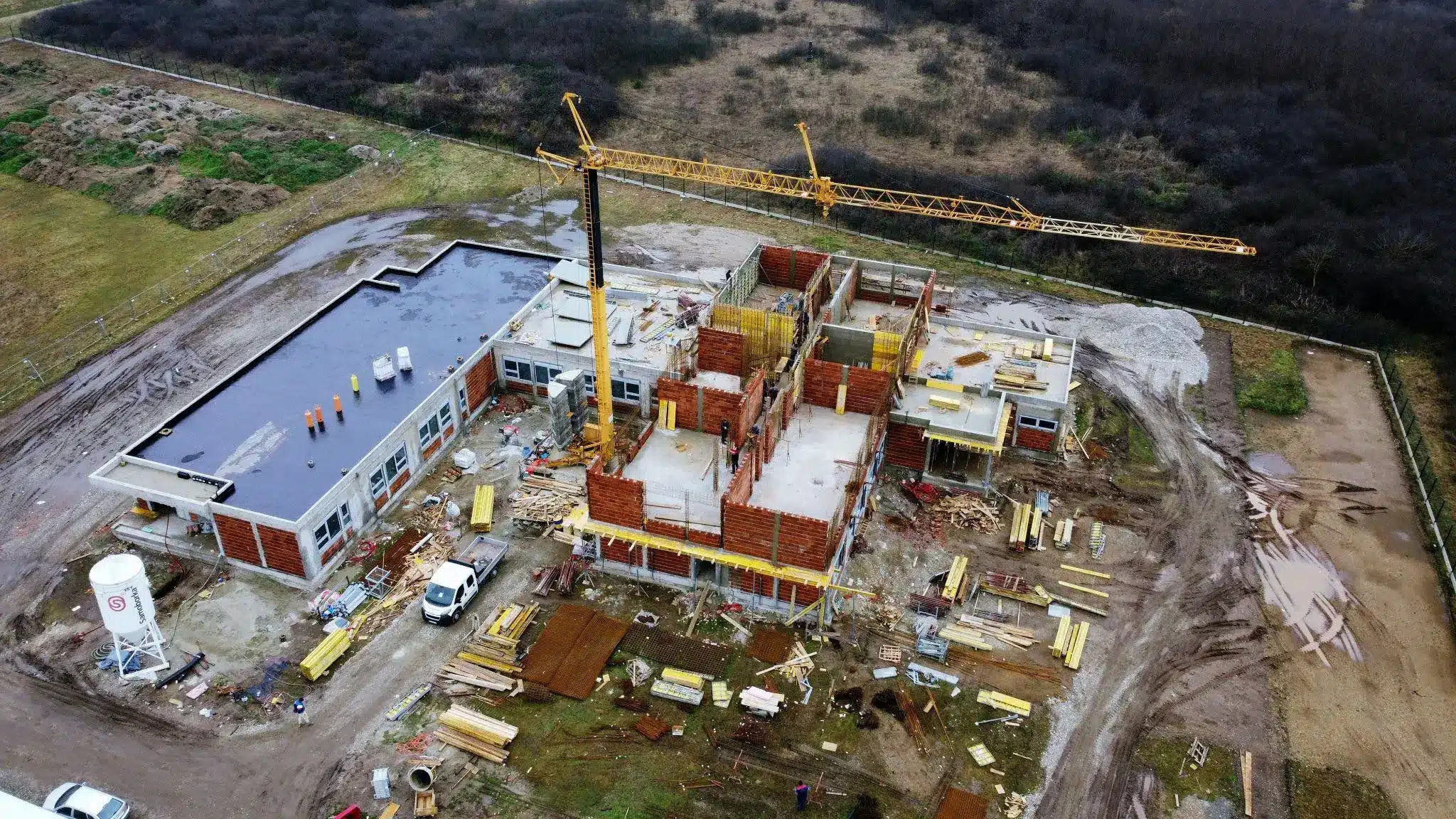 Construction site with crane and building framework in progress surrounded by muddy field and materials