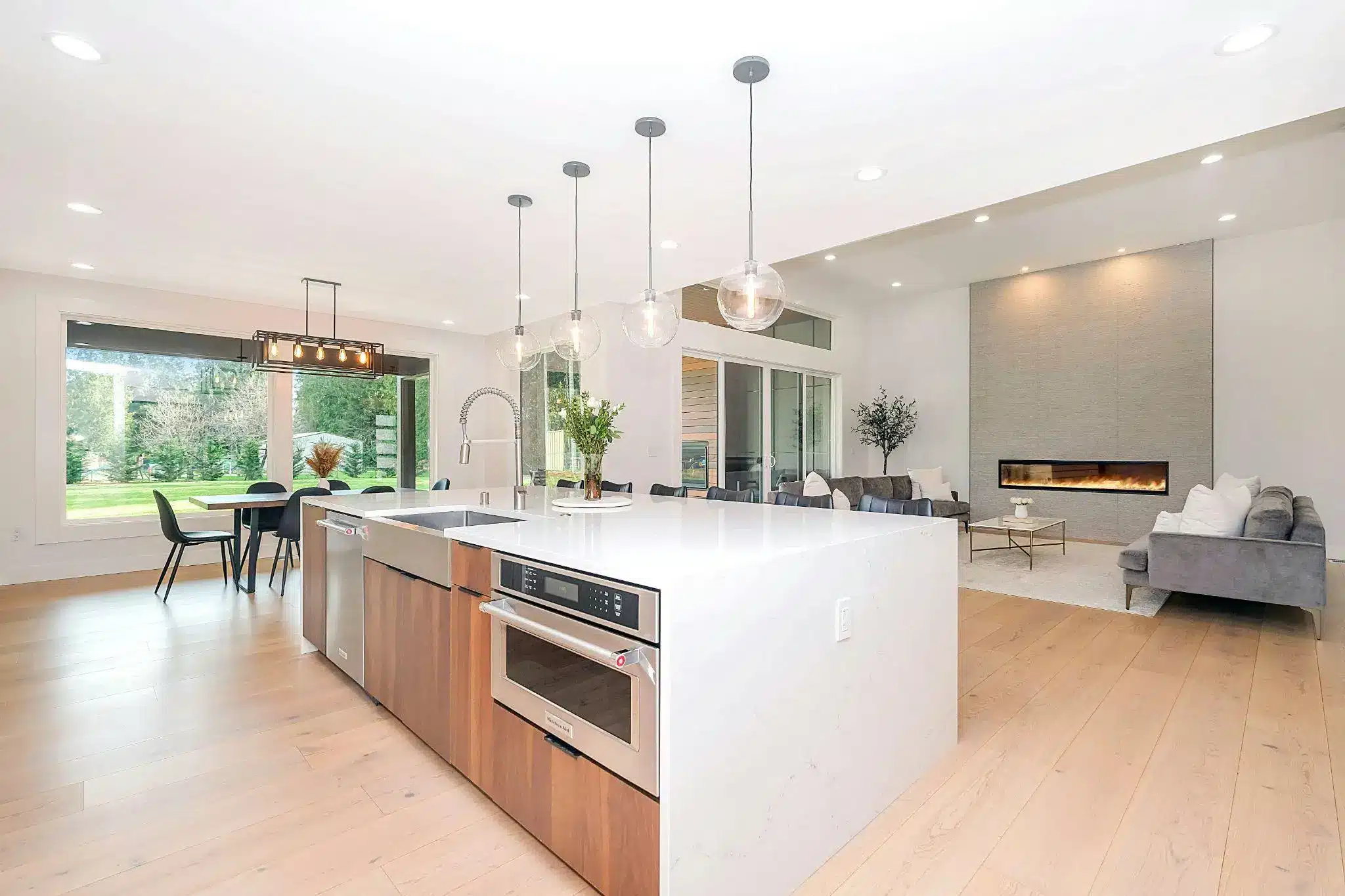 Spacious modern living area with open kitchen, island, large windows, and a wall-mounted fireplace