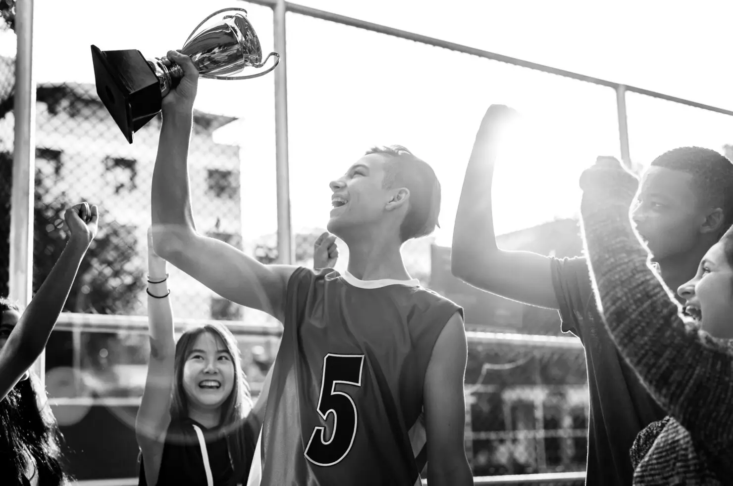 Teen celebrating with trophy outdoors surrounded by cheering friends in high contrast lighting