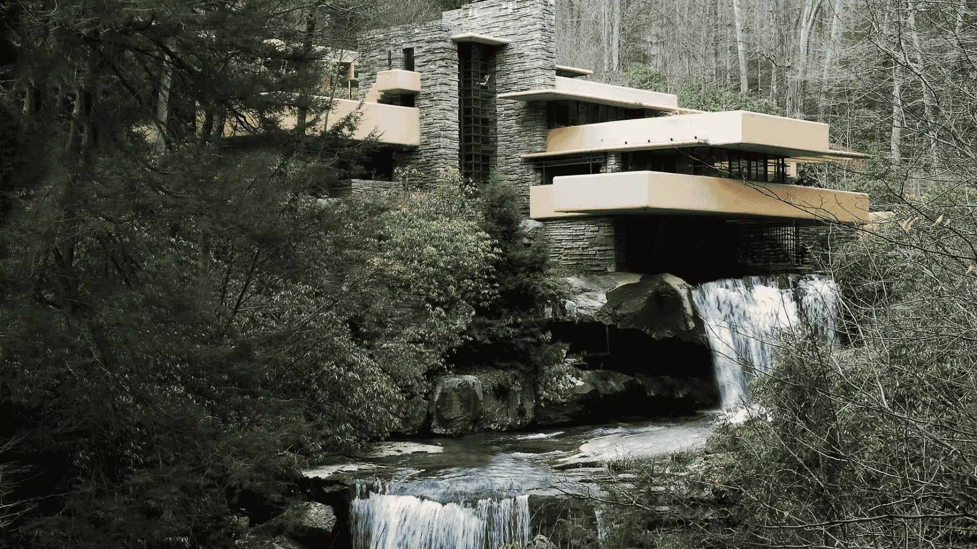 Fallingwater house designed by Frank Lloyd Wright, built over a waterfall surrounded by lush greenery and trees.