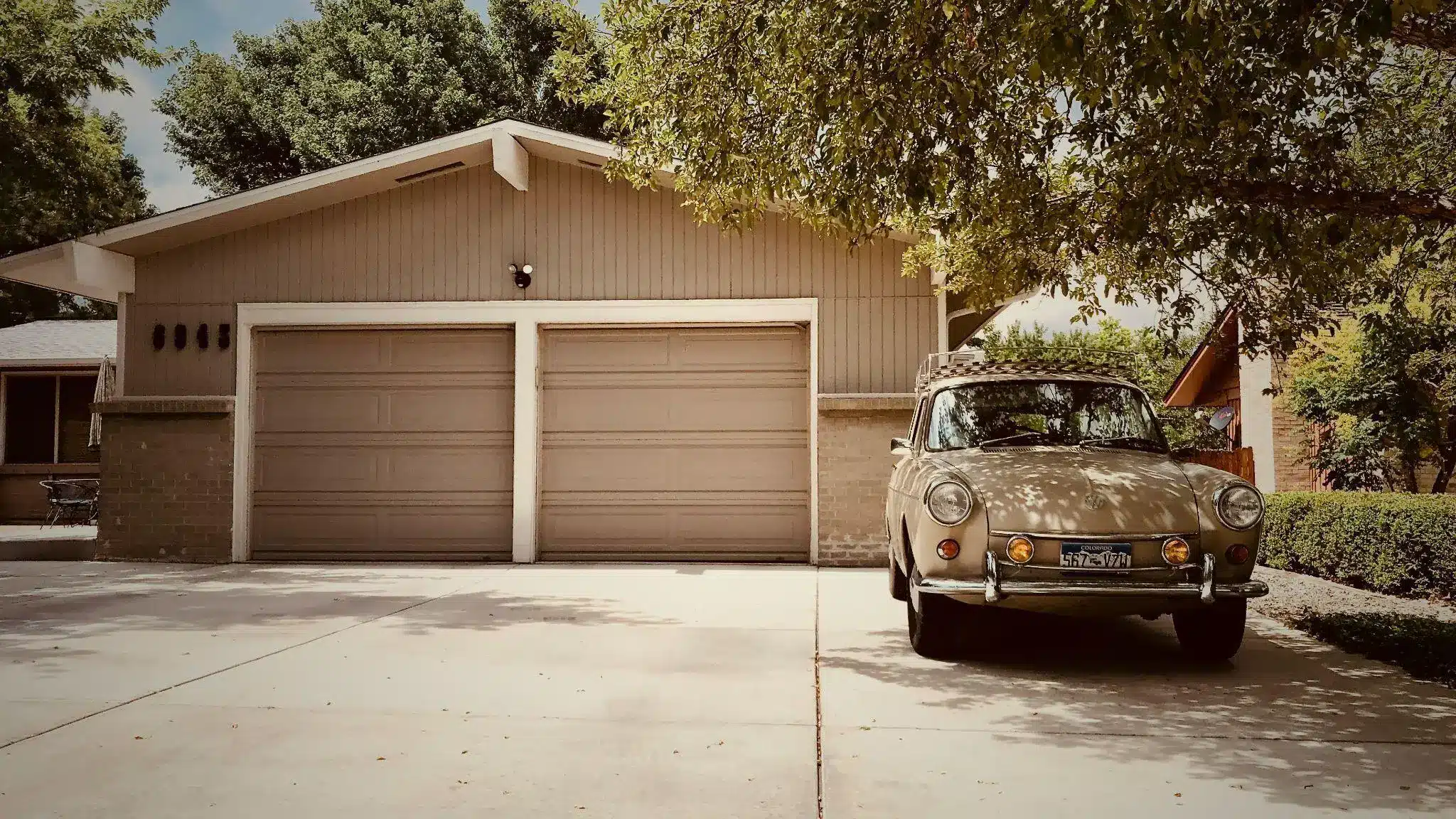 Vintage beige car parked in driveway of suburban house with double garage doors