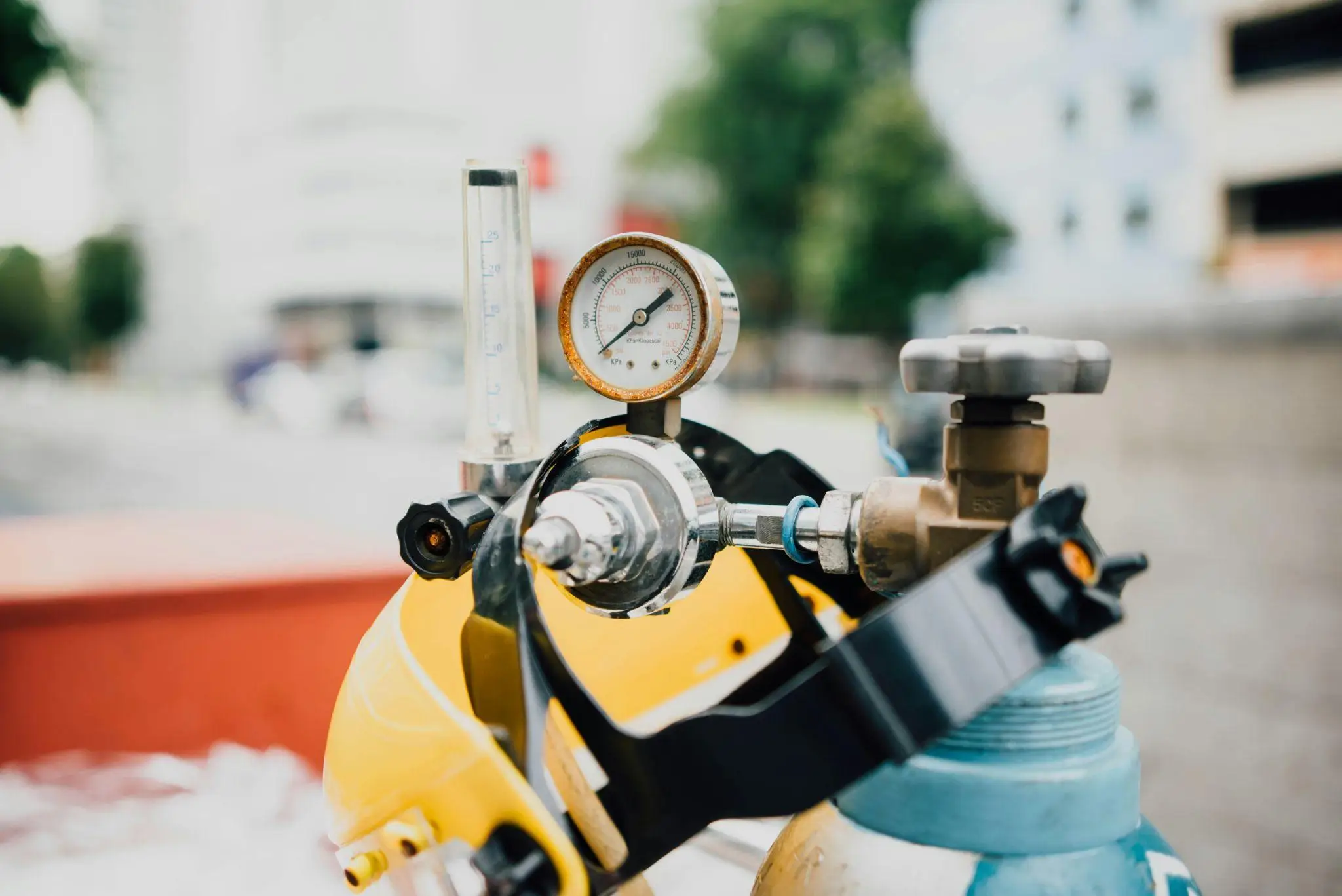 Close-up of gas regulator and pressure gauge on yellow and blue tank outdoors