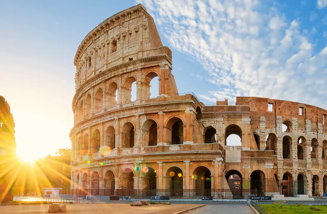 Colosseum illuminated by sunset with clear blue sky and scattered clouds in the background