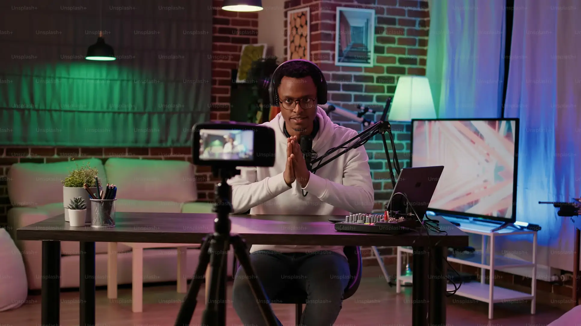 Podcaster wearing headphones speaking into microphone in colorful studio with camera setup