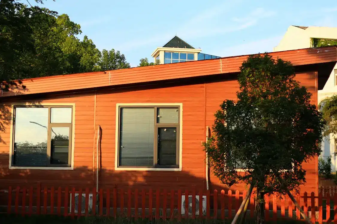 Red wooden building exterior with large windows and a small tree, under clear blue sky