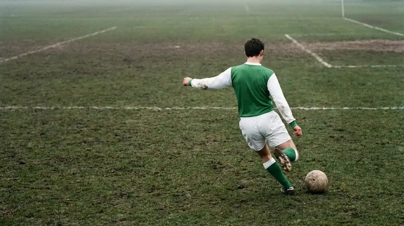 Soccer player in green jersey kicking ball on foggy, muddy field