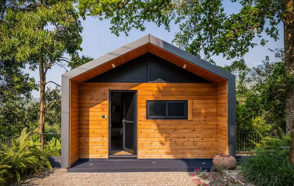 Wooden cabin with open door surrounded by lush greenery and bright sunlight