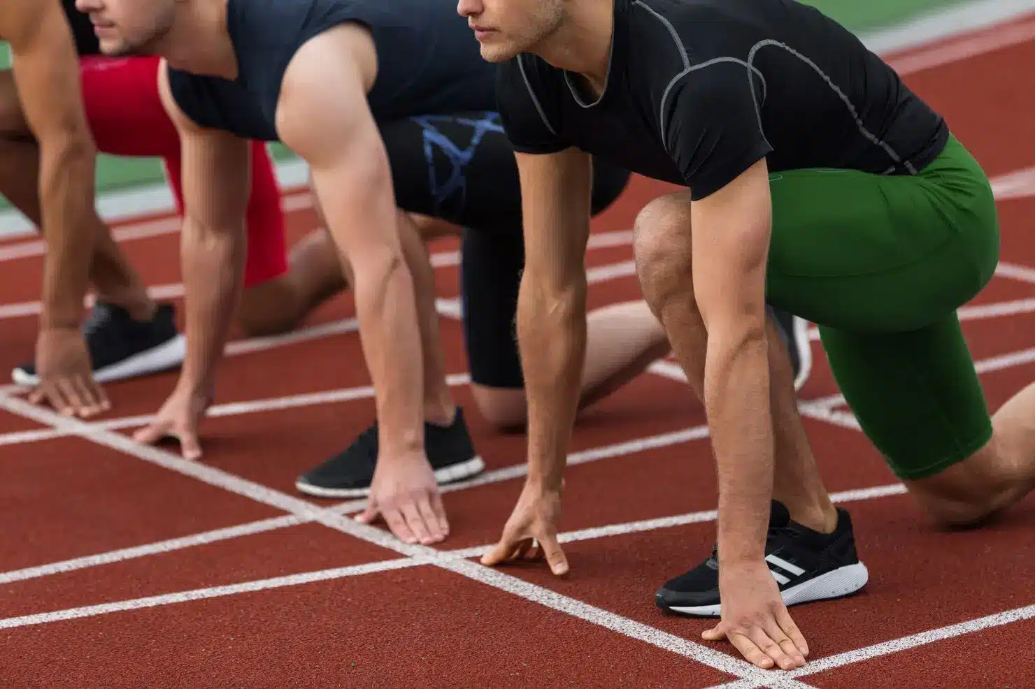 Athletes in starting positions on a red track wearing athletic gear