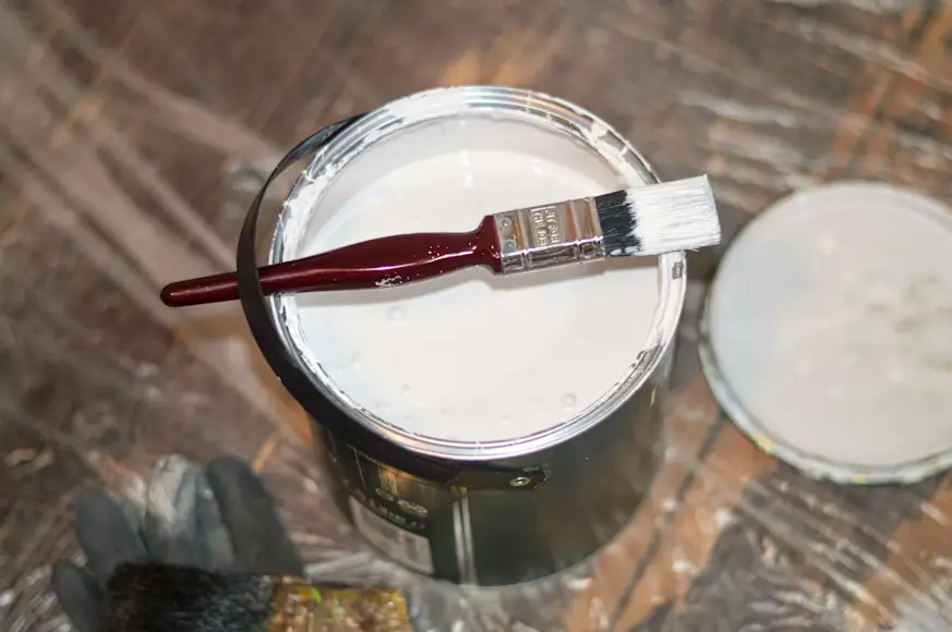 Open can of white paint with brush on lid in workshop setting