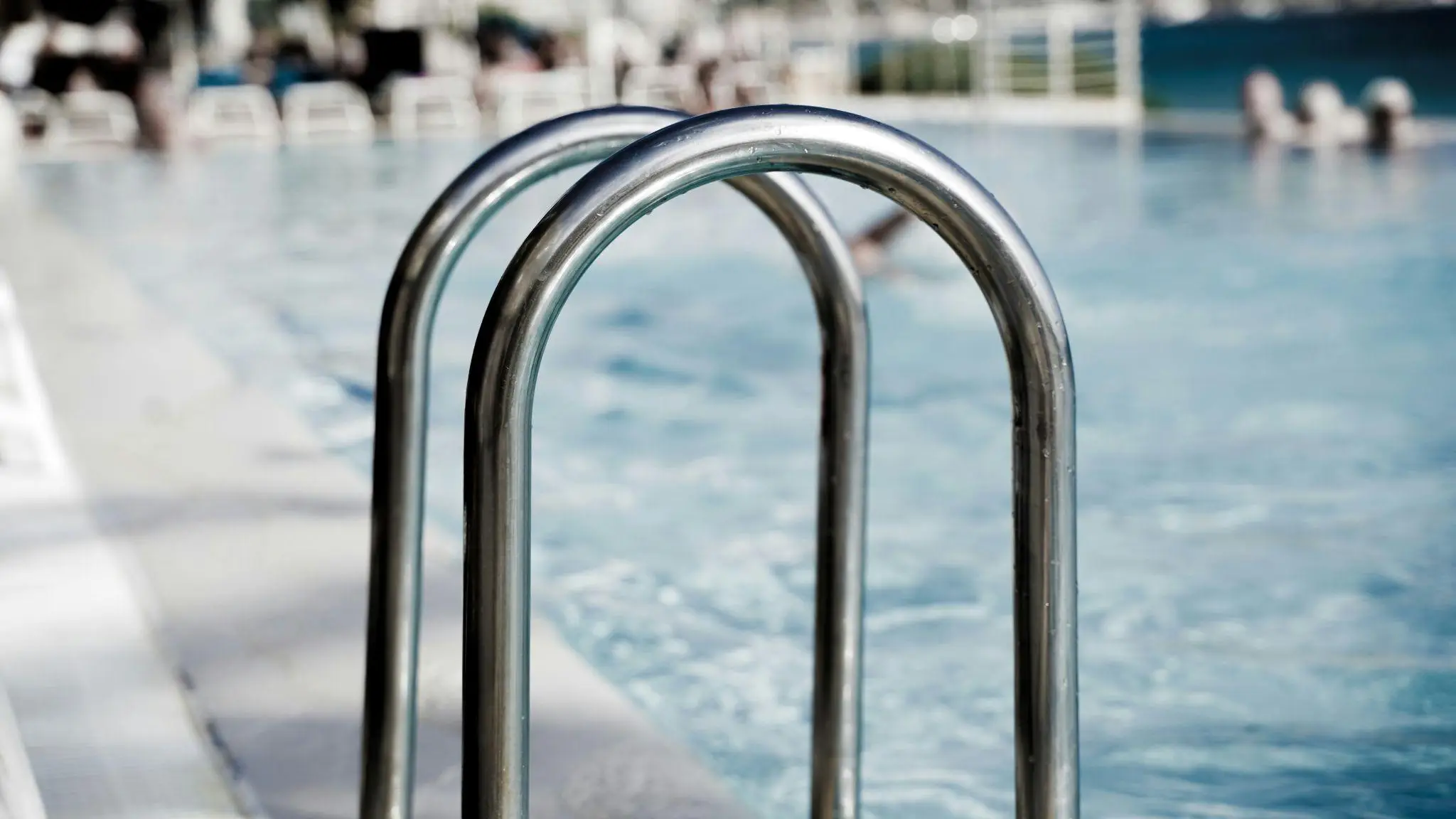 Stainless steel pool ladder leading into clear outdoor swimming pool water