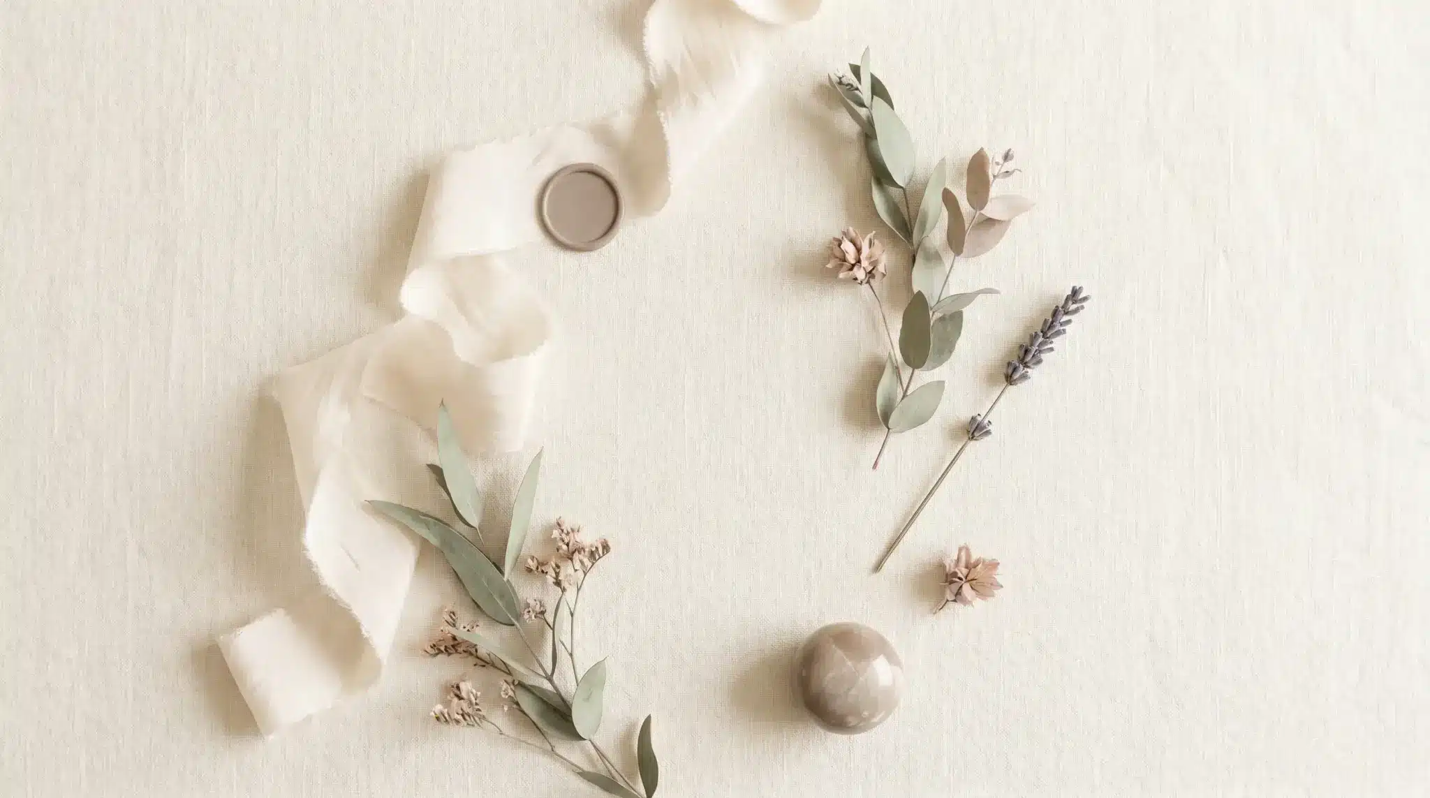 Delicate dried flowers and ribbon arranged on a light fabric surface with a marble sphere
