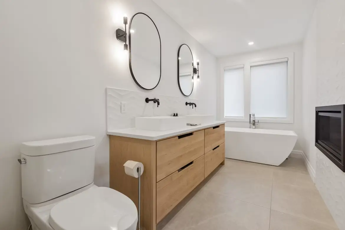 Modern bathroom with wooden vanity, double sinks, and freestanding tub under bright lighting